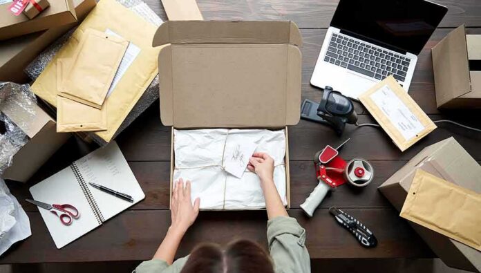 Person packing a cardboard box on a cluttered desk