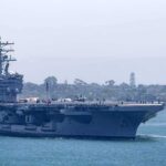 Aircraft carrier escorted by a tugboat in a harbor