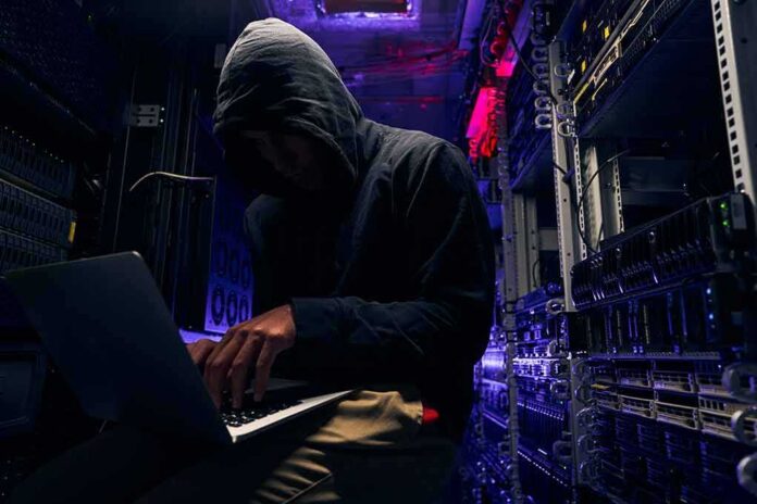 Hooded person using a laptop in a dark server room