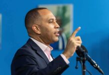 Man speaking at a microphone with raised finger