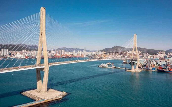 Cable-stayed bridge spanning a harbor with city skyline and mountains