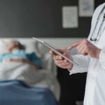 Home-Care Fraud Ring – Feds Move In Doctor using tablet beside hospital patient