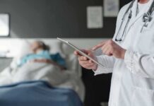 Home-Care Fraud Ring – Feds Move In Doctor using tablet beside hospital patient
