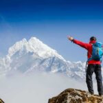 He Fell 500 Feet—Then Started Crawling Hiker with arms raised facing snowy mountain peak