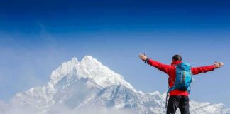 Hiker with arms raised facing snowy mountain peak