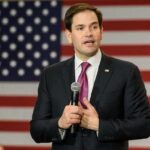 A Blunt Border Warning Is Echoing Across Europe man in suit speaking with microphone before American flag