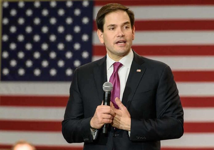 shutterstock_375031762 man in suit speaking with microphone before American flag