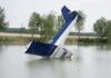 An abandoned aircraft partially submerged in a calm body of water surrounded by trees
