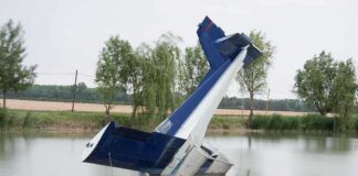 An abandoned aircraft partially submerged in a calm body of water surrounded by trees