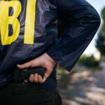FBI’s COVID Fraud Fugitive Finally Caught FBI agent in jacket drawing a handgun