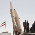 Soldiers stand beside large missiles at an outdoor display