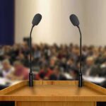 This Campus Speech Fight Came With A Price Podium with two microphones facing a blurred audience