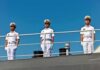 three naval officers in white uniforms standing on a ship deck