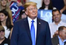 Donald Trump at a rally wearing a dark suit and blue tie