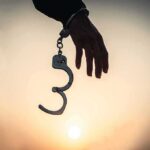 Hand with open handcuff in silhouette at sunset