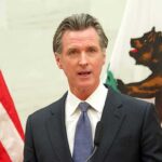 Gavin Newsom speaking at a podium with U.S. and California flags behind him
