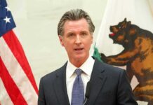 Homeless Cash Mystery – Oversight Killed Gavin Newsom speaking at a podium with U.S. and California flags behind him
