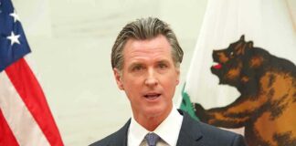 Gavin Newsom speaking at a podium with U.S. and California flags behind him