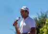 Man in white cap speaking into a microphone outdoors
