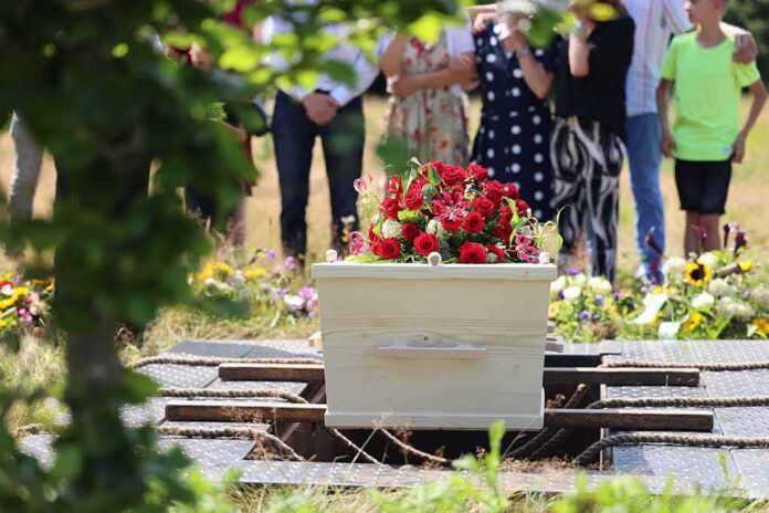 shutterstock_2368329541-1 White coffin with red flowers at outdoor burial