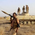 soldier carrying rocket-propelled grenade launcher in front of armored vehicle