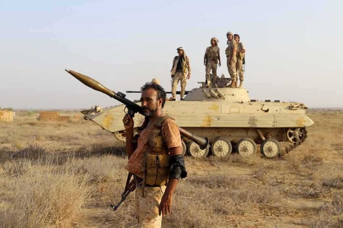 soldier carrying rocket-propelled grenade launcher in front of armored vehicle