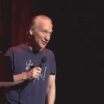 Bill Maher performing stand-up with a microphone on stage